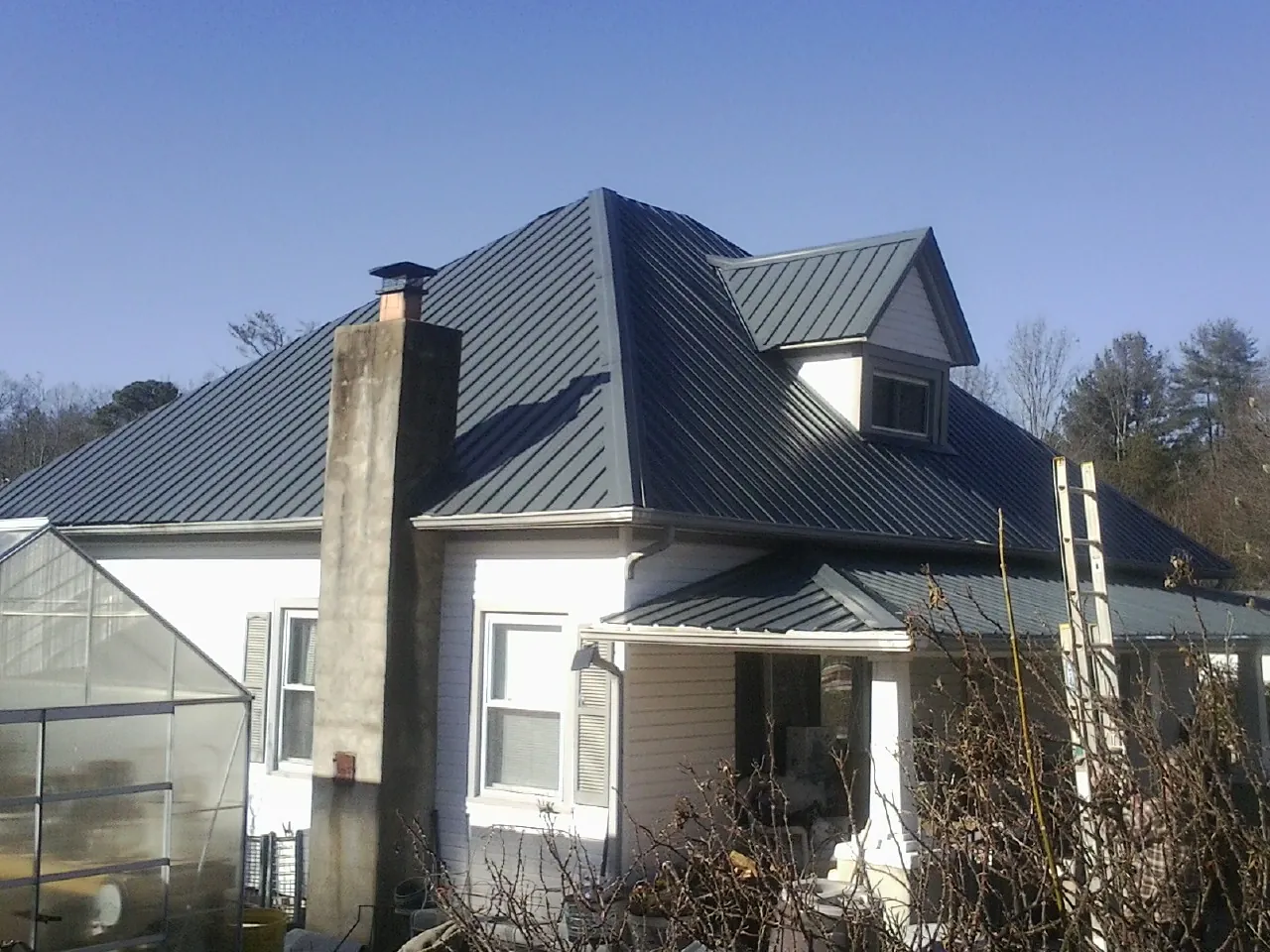 Dark blue standing seam metal roof on a white farmhouse with dormer — Slate & Tile Roof Repair by Roofing Brothers in Turners Station