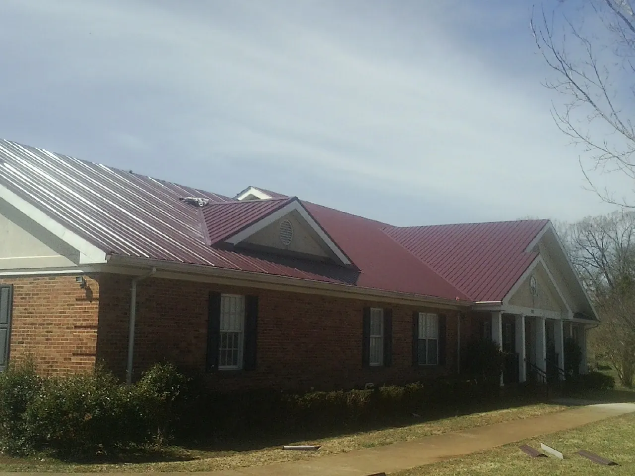 Red metal roof with gabled entries on a long brick building, from a Hail Damage Roof Repair job in Turners Station