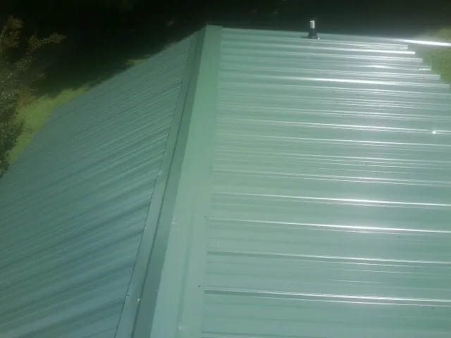 New green metal panels meeting at the ridge of a roof — Flat Roof Repair work by our crew in Turners Station