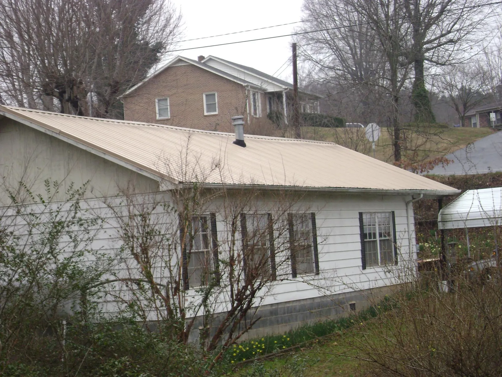 Tan metal roof on a white sided house set into a hillside — Commercial Roofing by Roofing Brothers in Turners Station